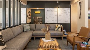 A modern living room with a sectional sofa, a wooden coffee table with books, a map on the wall, and a lamp. - Mountain Modern Sedona, Tapestry Collection by Hilton (Sedona)