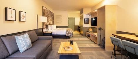A hotel room with a sofa, a small table, a bed, a desk, and a chair.