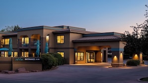 A hotel entrance with a sign indicating the direction to the entrance, a covered outdoor seating area, and a well-lit facade. - Mountain Modern Sedona, Tapestry Collection by Hilton (Sedona)