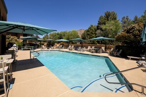 A rectangular swimming pool with blue lane markings, surrounded by lounge chairs and umbrellas, with trees and a building in the background. - Mountain Modern Sedona, Tapestry Collection by Hilton (Sedona)