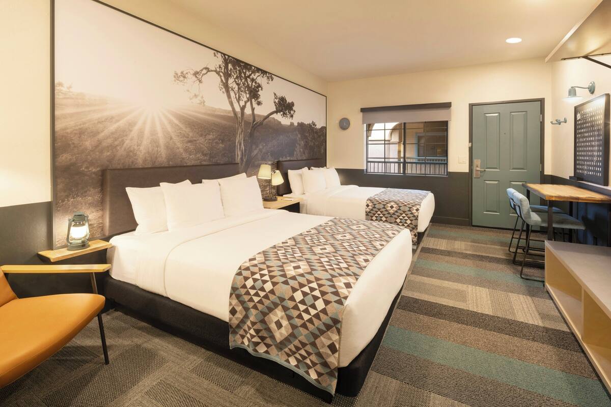Une chambre d’hôtel avec un grand lit, un bureau, une chaise, une table de chevet et une lampe fixée au mur.
