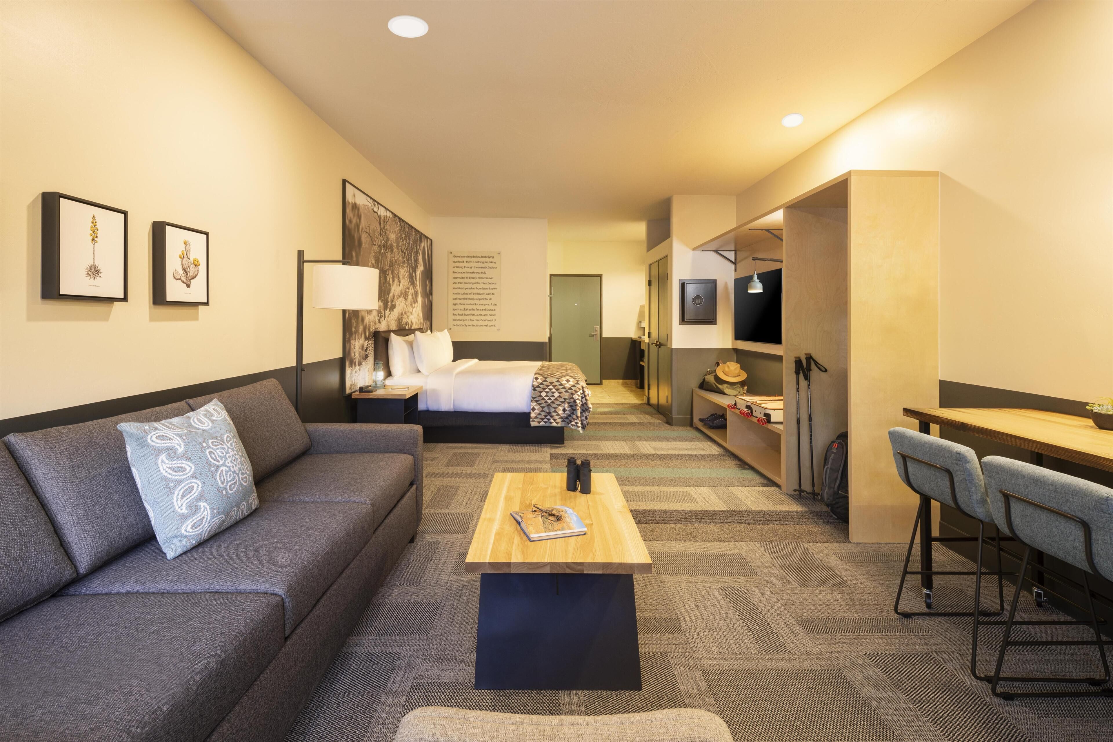 A hotel room with a sofa, a small table, a bed, a desk, and a chair.