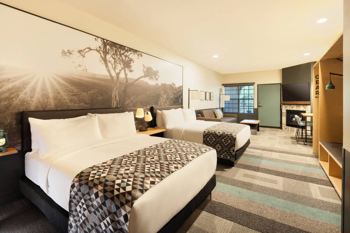 Une chambre d’hôtel avec un grand lit, un lit plus petit, un bureau, une télévision et une bibliothèque.