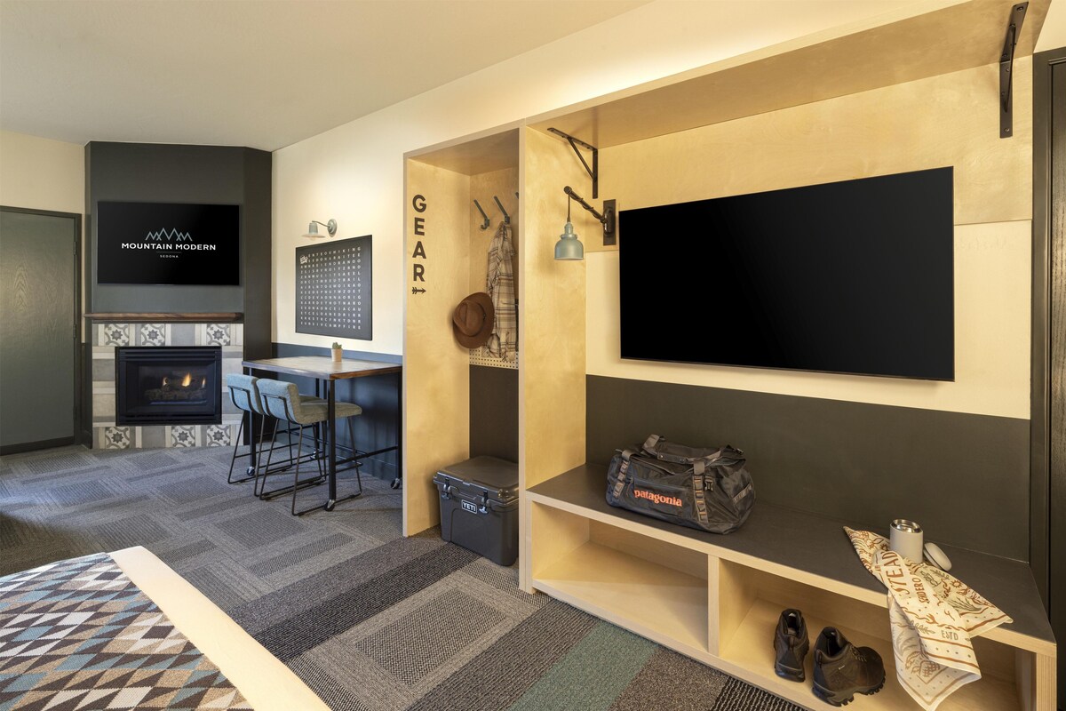 A modern living room with a fireplace, a TV mounted on the wall, a dining area with a table and chairs, and a shoe rack with boots and a bag.