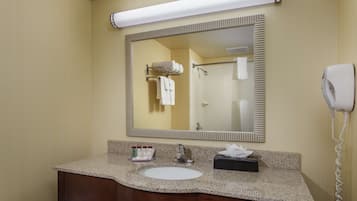 A hotel bathroom with a granite countertop sink, a mirror, a towel rack, a hair dryer, and a bottle of hand soap.