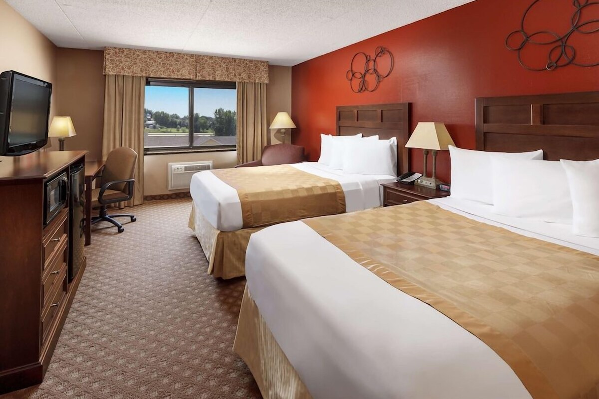 A hotel room with two beds, a desk with a television, a chair, and a window with curtains.