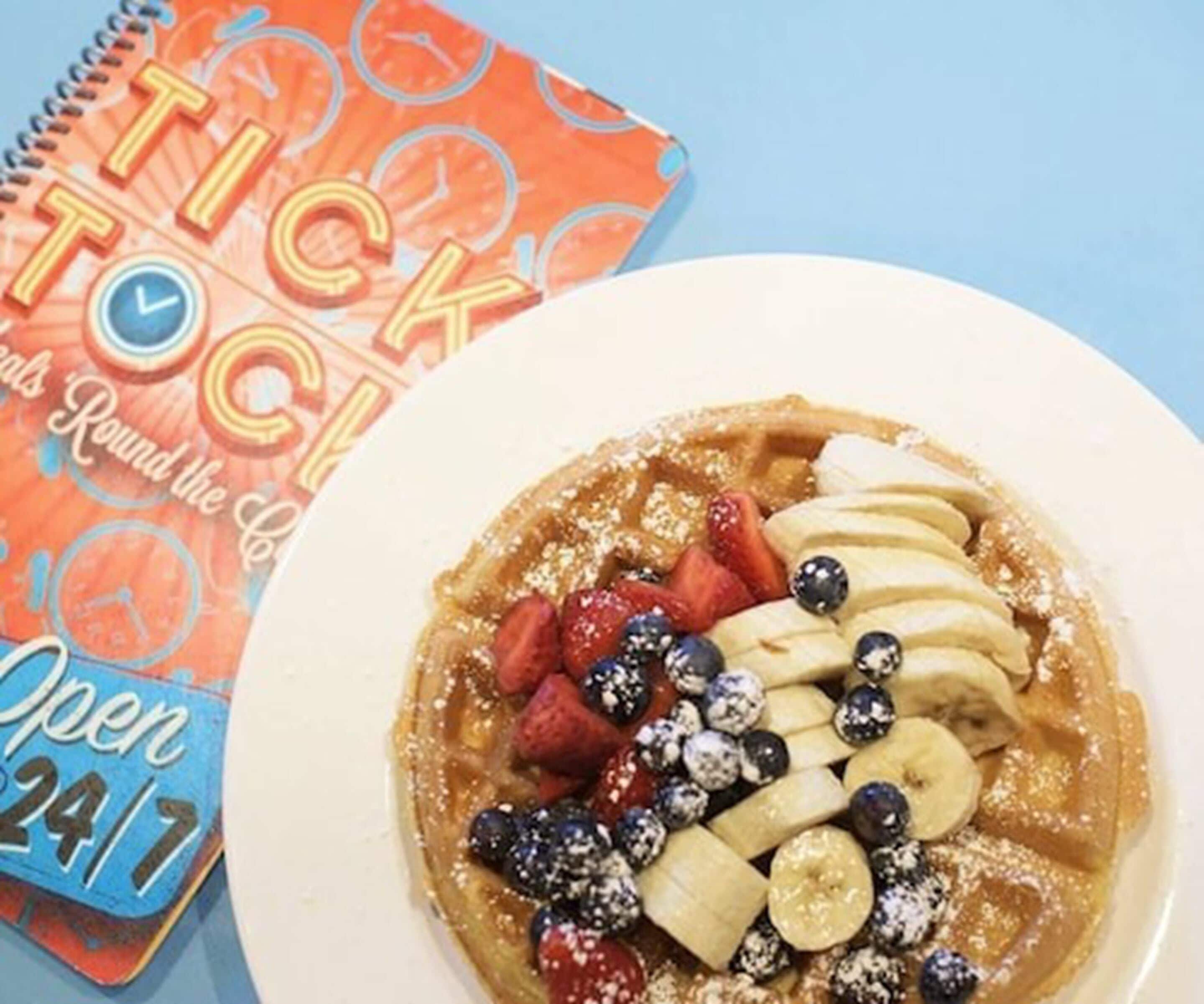 A plate of waffles topped with strawberries, blueberries, banana slices, and powdered sugar.