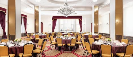 A banquet hall with round tables, chairs, and a chandelier.