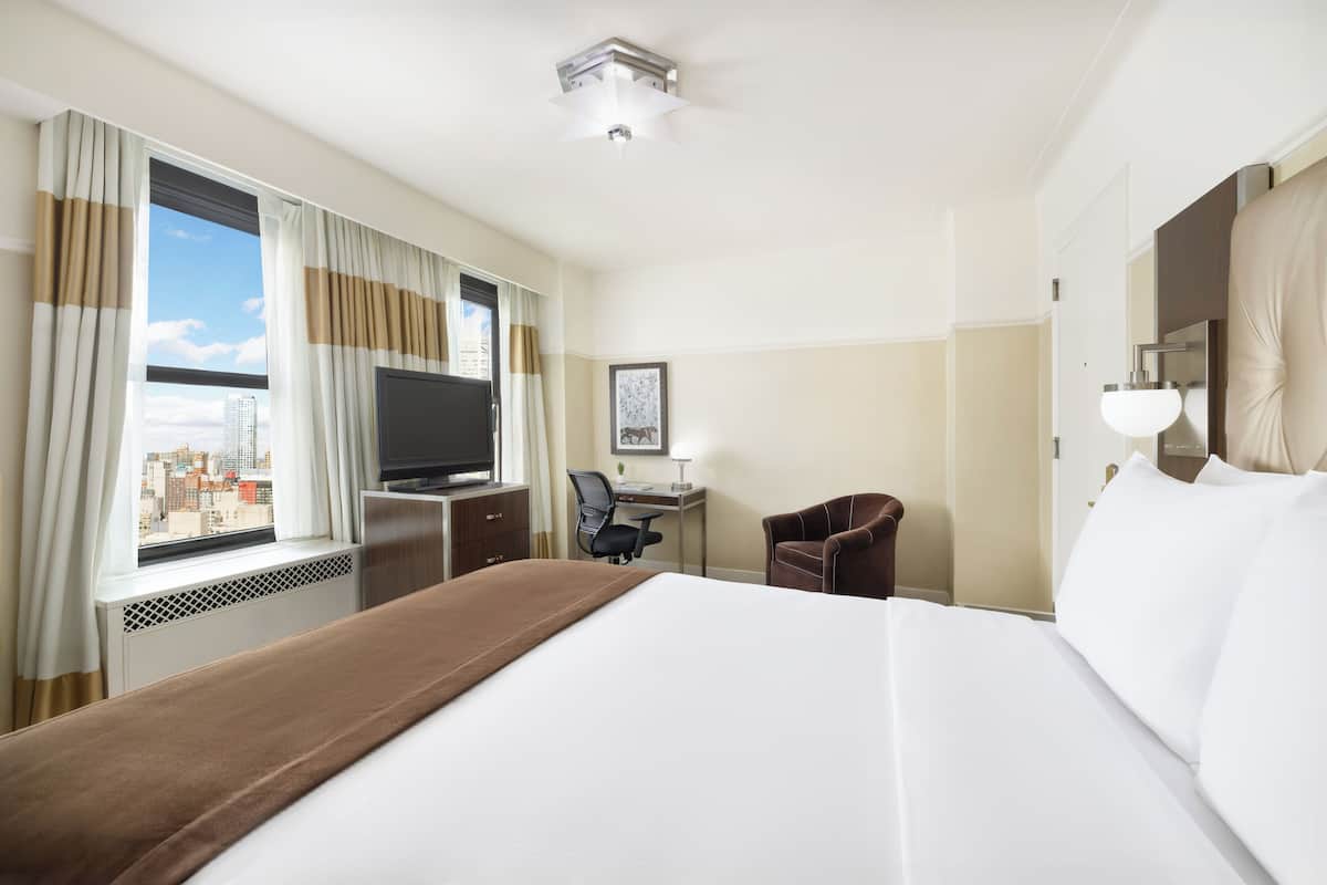 A hotel room with a large bed, a desk with a chair, a television, and a window with curtains.
