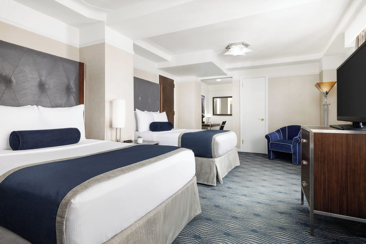 A hotel room with two beds, a desk, a chair, a television, and a large mirror.