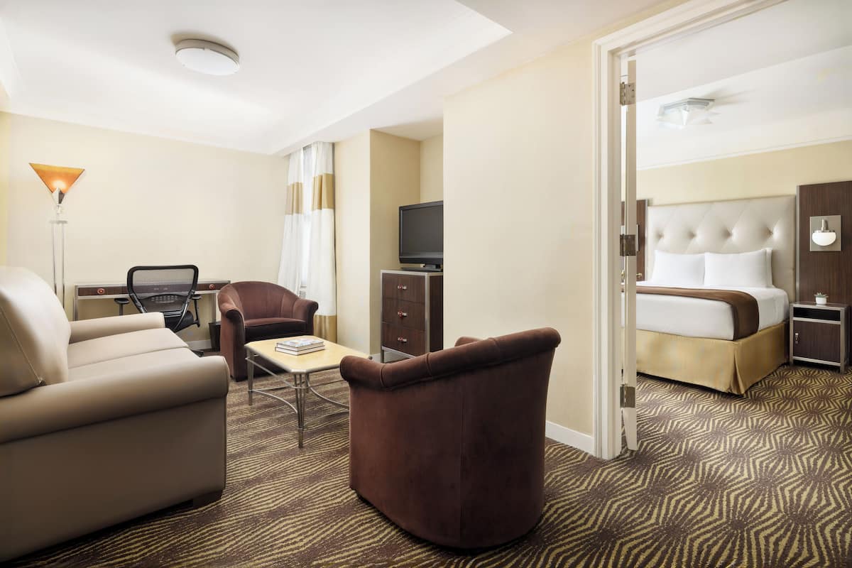 A hotel room with a bed, a sofa, a chair, a desk, and a television.
