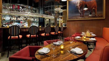 Zona de bar con varias estanterías llenas de botellas de licor, taburetes y un cuadro grande de un toro en la pared.