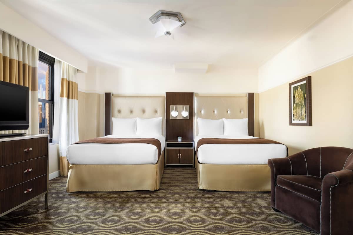 A hotel room with two beds, a TV, a desk, and a chair.