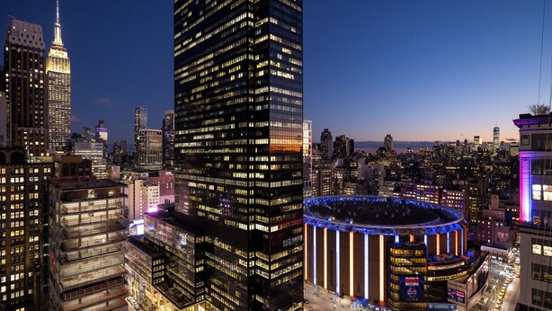 A cityscape with high-rise buildings, including a prominent skyscraper with illuminated windows and a circular building with a central atrium. - NEW YORKER BY LOTTE HOTELS (New York)