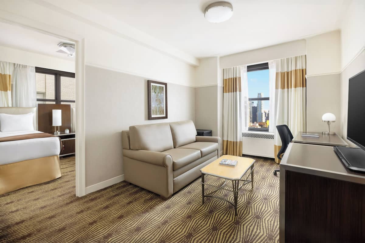 A hotel room with a bed, a sofa, a desk, and a view of the city.