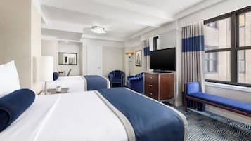 A hotel room with two beds, a desk, a TV, and a large window with curtains.