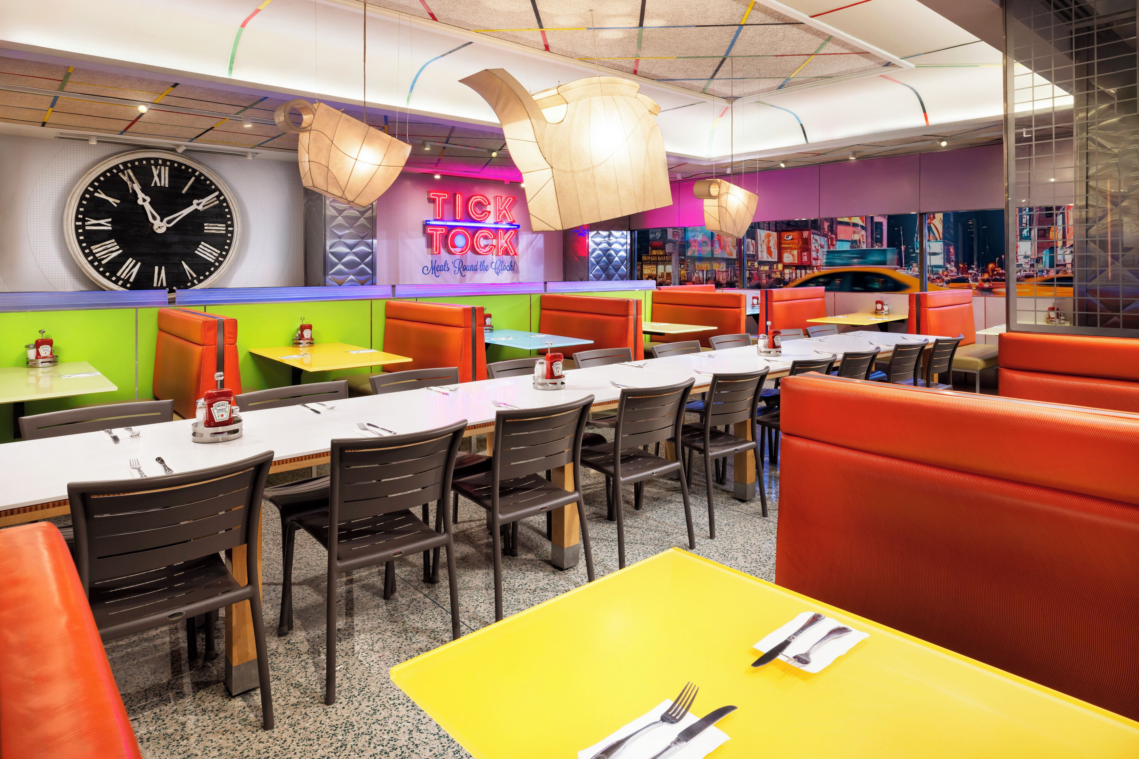 Un restaurante con cabinas y mesas, un reloj grande y un letrero de neón.