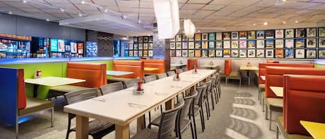 Un restaurante con cabinas y mesas, techo colorido y obras de arte en las paredes.