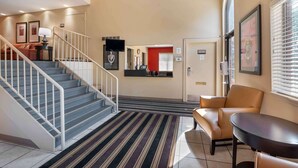 A hotel lobby with a staircase, a reception desk, a seating area, and a framed artwork on the wall. - Studio 6 Corporate Extended Stay Indianapolis, IN - North Carmel (Carmel)