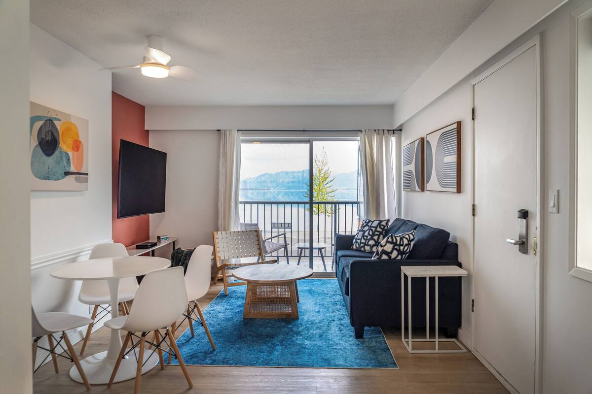A modern living room with a blue rug, white furniture, a black sofa, and a view of the outdoors.