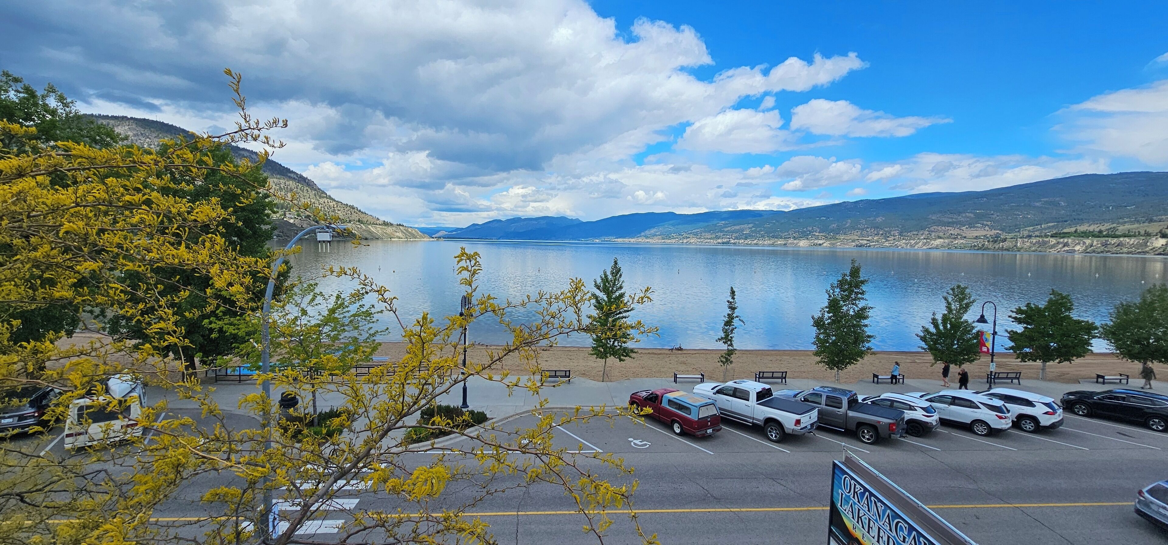 Un parking avec des véhicules, et une vue sur un lac et des montagnes.
