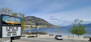 A sign for Okanagan Lakefront Resort with a view of a lake and mountains.