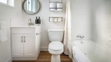 Un baño moderno con un lavamanos, inodoro y bañera blancos. Hay repisas sobre el inodoro con artículos de aseo.