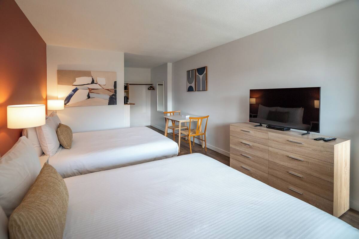 A hotel room with two beds, a desk, a chair, a TV, and a dresser.