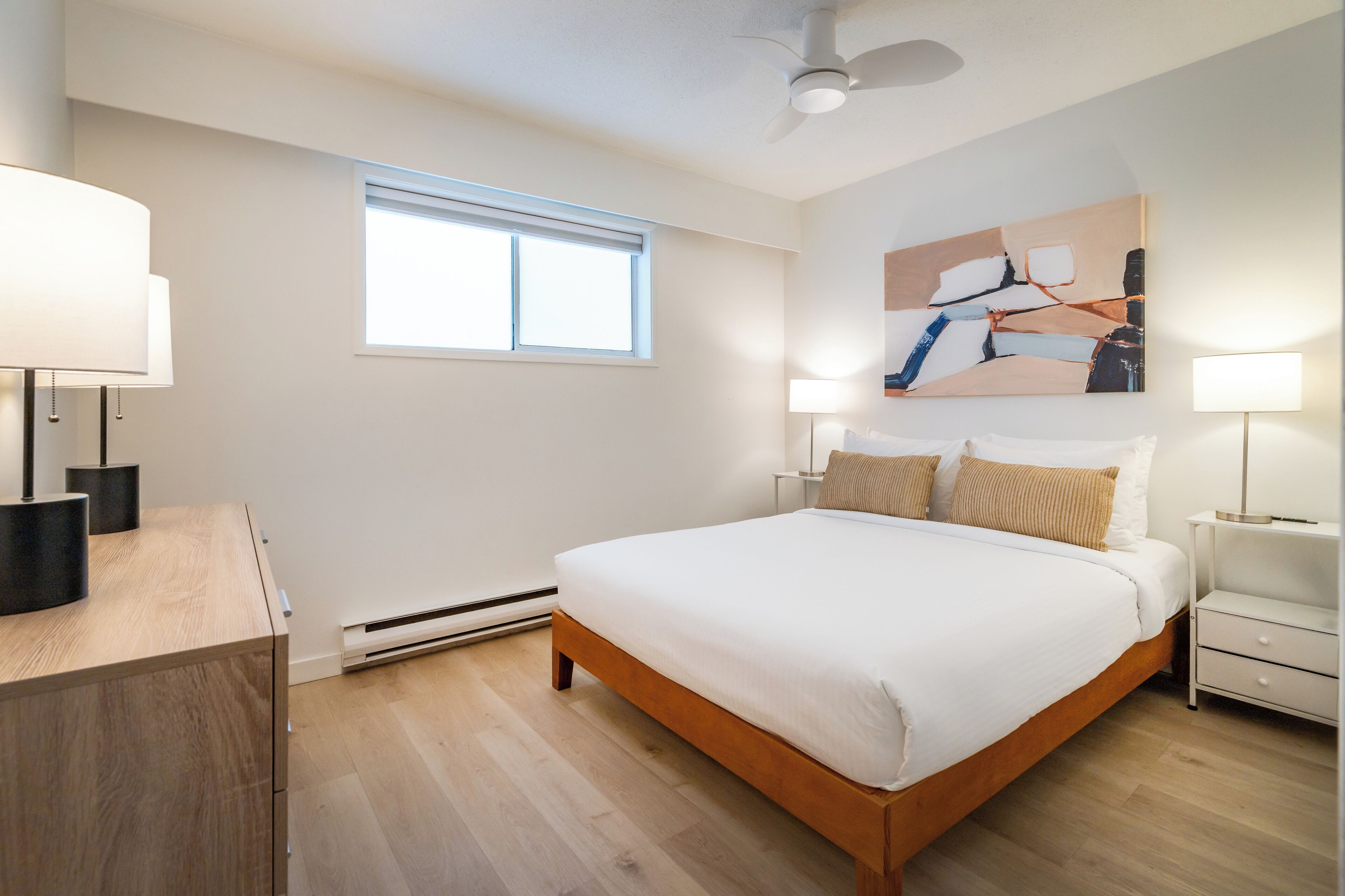 A bedroom with a bed, bedside tables, a desk, a window, and a ceiling fan.