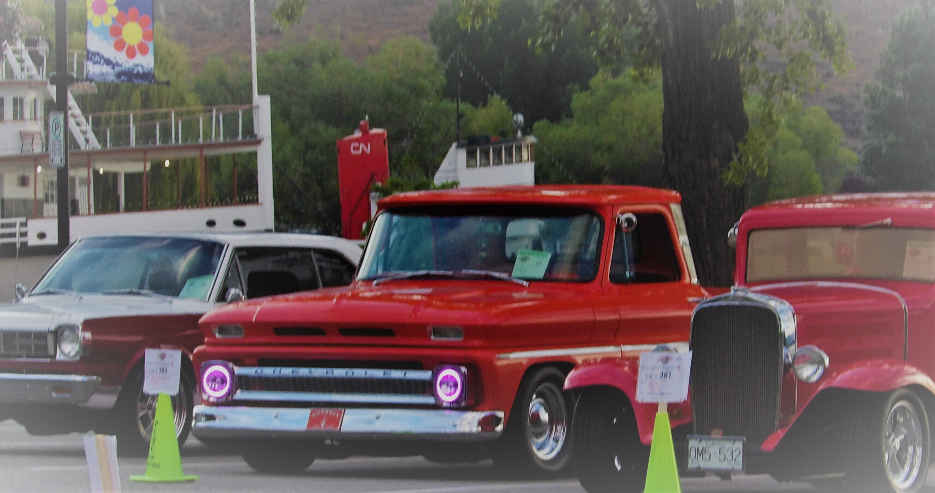 Um carro vermelho antigo estacionado num estacionamento, com um edifício ao fundo.