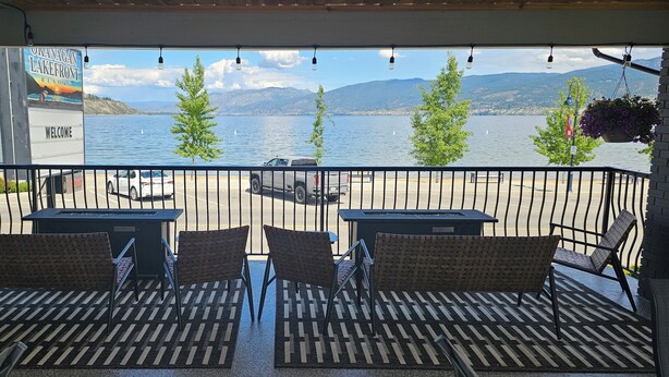 Een overdekt terras met tafels en stoelen, met uitzicht op een meer en bergen op de achtergrond.