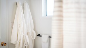 Een badkamer met twee witte handdoeken aan een zwarte handdoekhouder, een witte deur en een raam met zonwering.