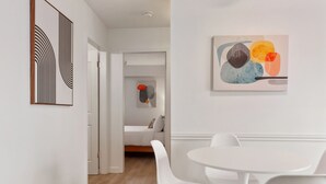 Una habitación moderna y minimalista con una mesa y sillas blancas para comer, un sofá y arte abstracto en la pared.
