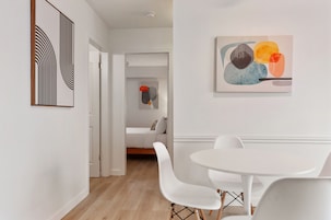 A modern, minimalist room with a white dining table and chairs, a sofa, and abstract wall art.