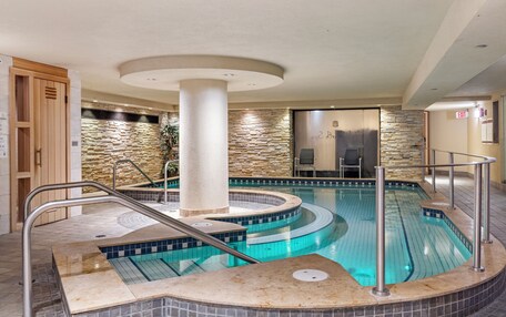 A swimming pool with a stone wall and a circular hot tub area.