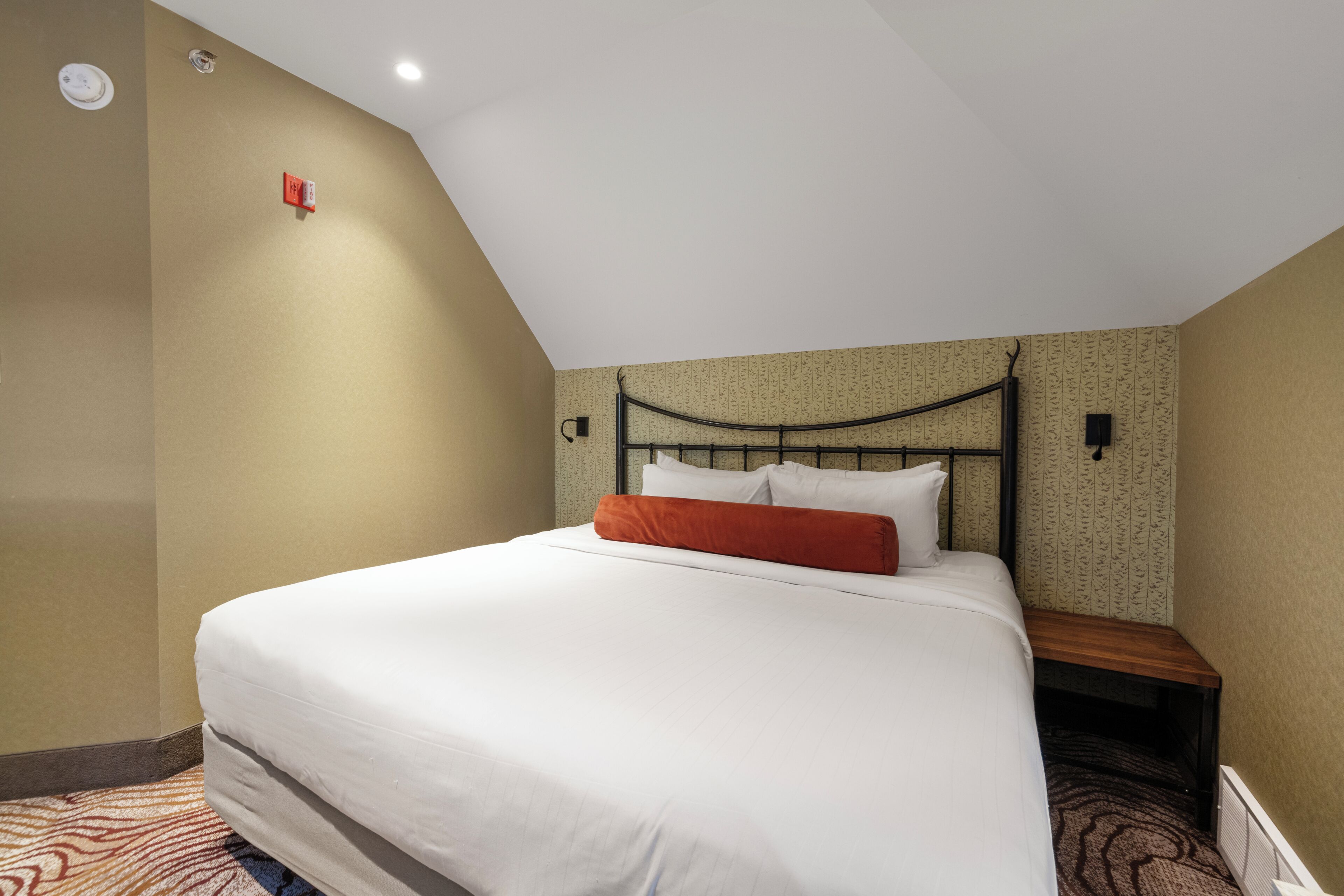 A hotel room with a single bed, a nightstand, a wall-mounted lamp, and a ceiling light.