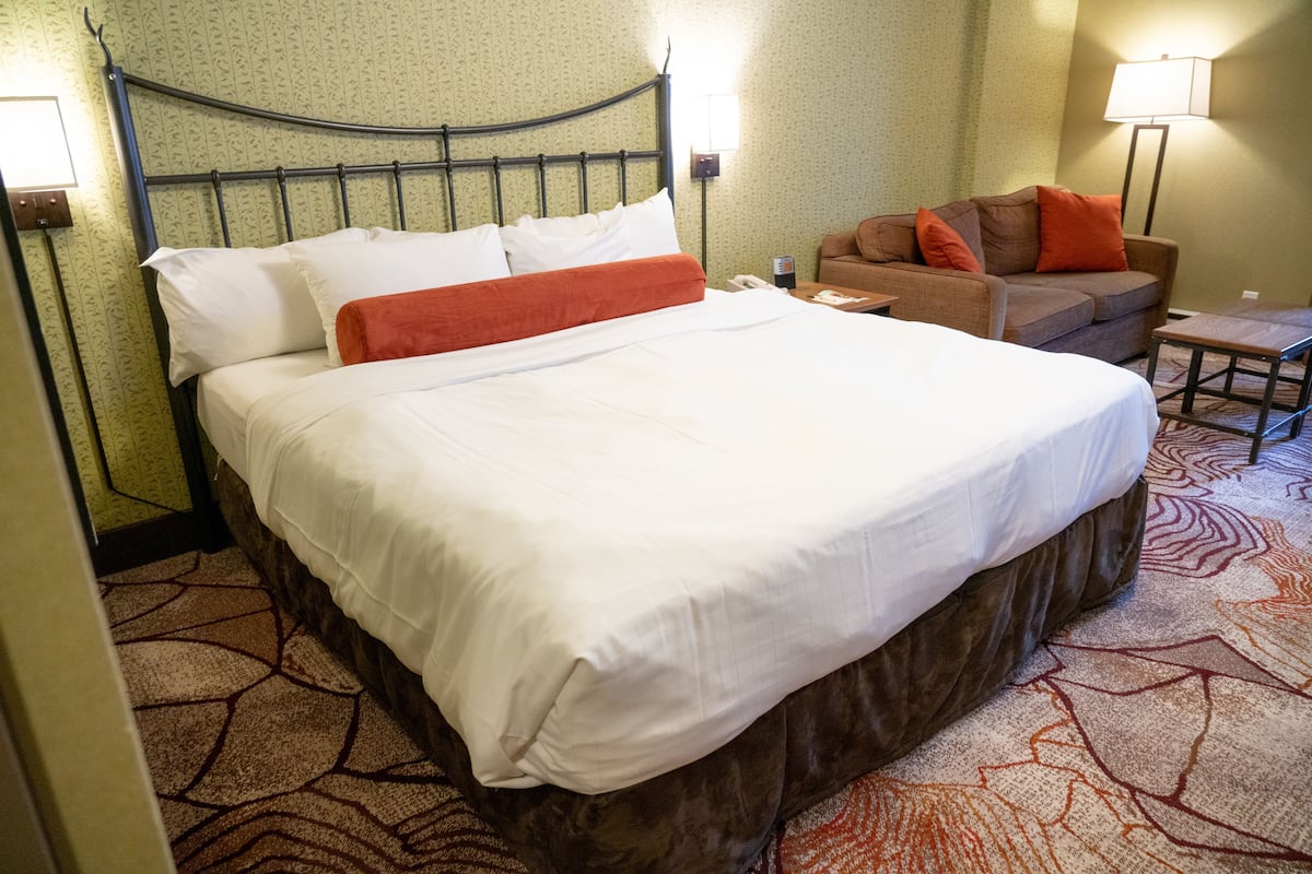 Una habitación de hotel con una cama grande, un sofá, una mesita y una lámpara.