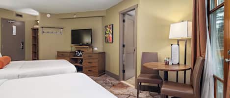 A hotel room with two beds, a television, a desk with a chair, a coffee machine, and a window with curtains.