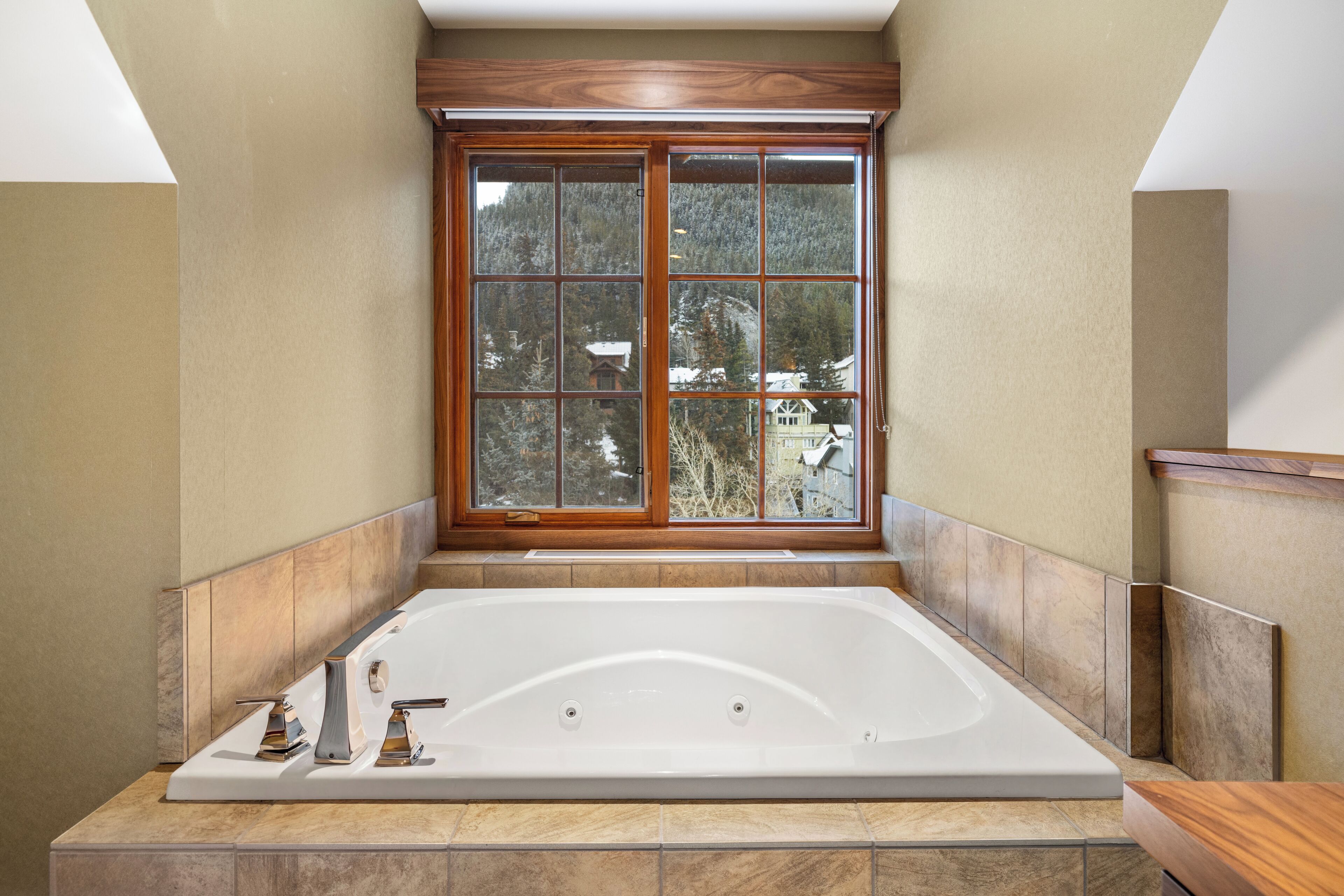 Un baño con una bañera grande, una ventana con vista a árboles y paneles de madera.