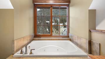 Un baño con una bañera grande, una ventana con vista a árboles y paneles de madera.