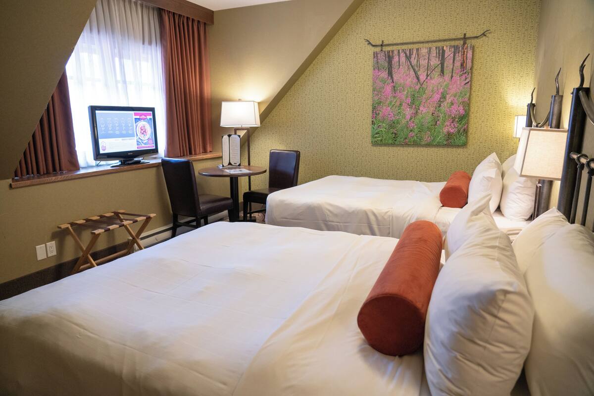Una habitación de hotel con dos camas, un escritorio con una computadora, una silla y un cuadro en la pared.