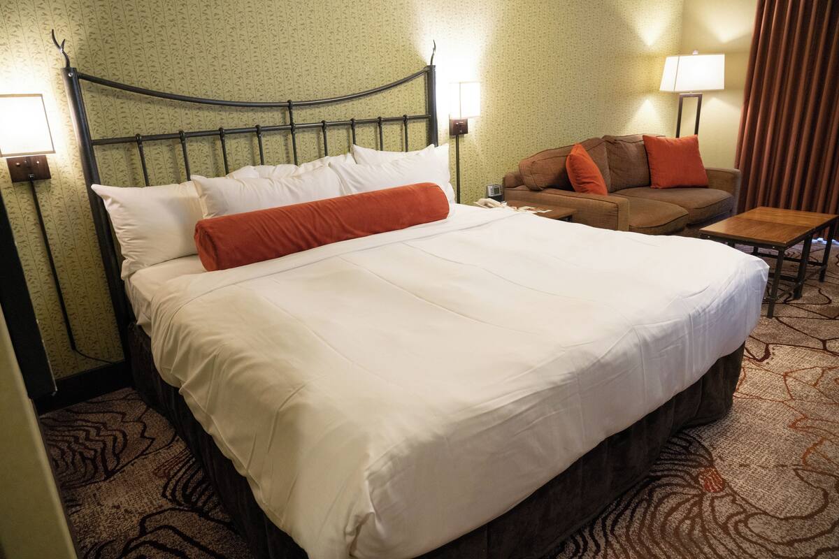 Una habitación de hotel con una cama grande, un sofá, una mesita y dos lámparas.