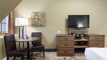 Une chambre d’hôtel avec un lit, un bureau et une chaise, un téléviseur, un tableau au mur et une fenêtre avec des rideaux.