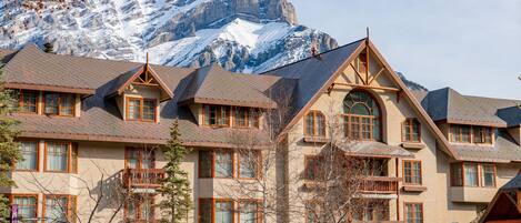 Un hotel de varios pisos con estilo arquitectónico tradicional, que cuenta con balcones y ventanas amplias, frente a un paisaje de montañas nevadas.