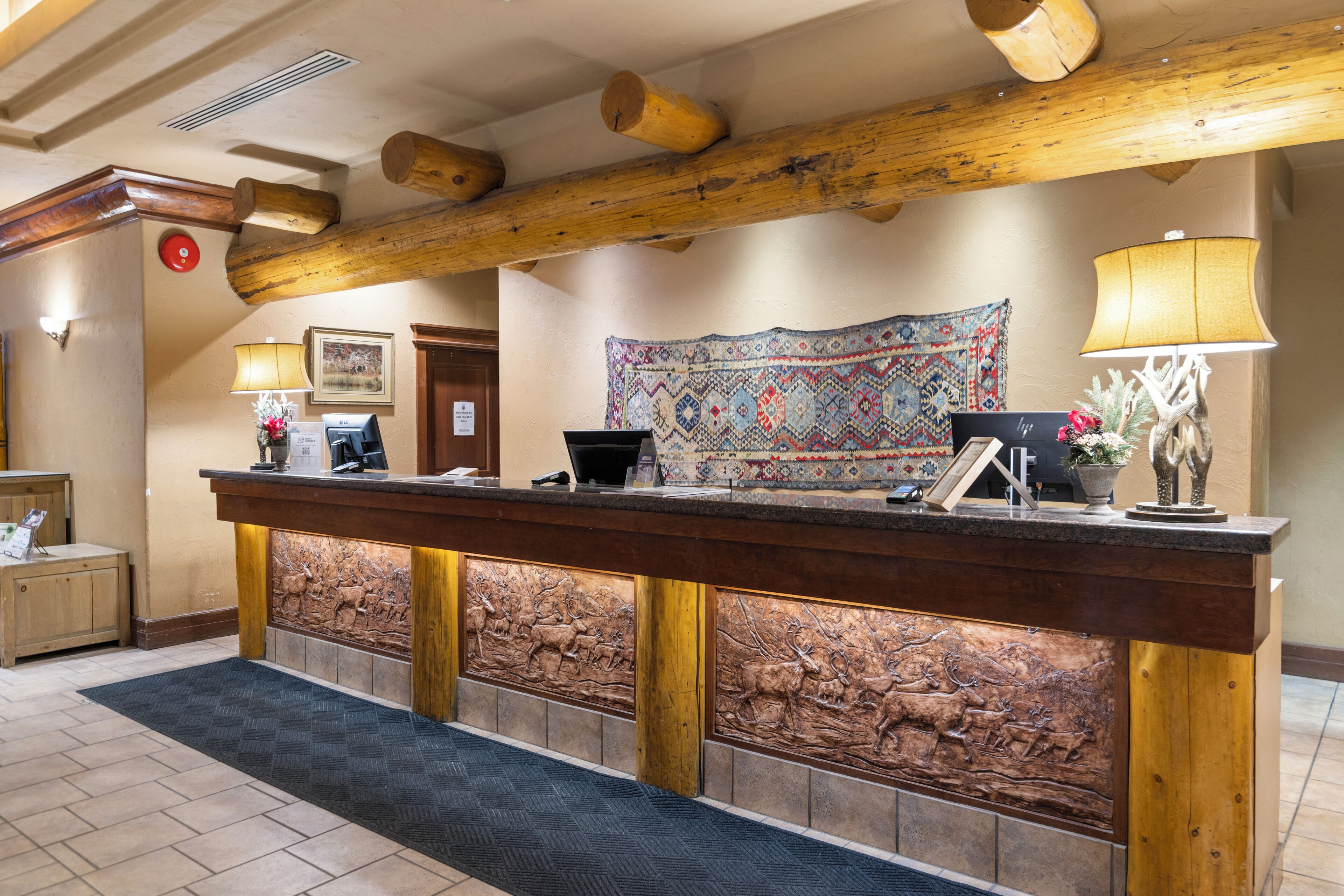 A reception desk with a wooden frame, a patterned tapestry, and a lamp.