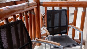 Deux chaises dotées d’une structure en métal et d’un dossier en treillis, placées sur un balcon orné de rampes en bois, d’où l’on peut admirer un paysage montagneux.