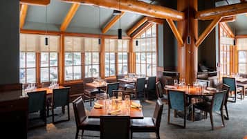 A restaurant with wooden beams, large windows, and tables set for dining.