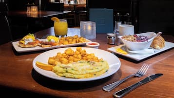 A breakfast table with plates of eggs, potatoes, and a croissant, along with a glass of orange juice and a bowl of fruit.