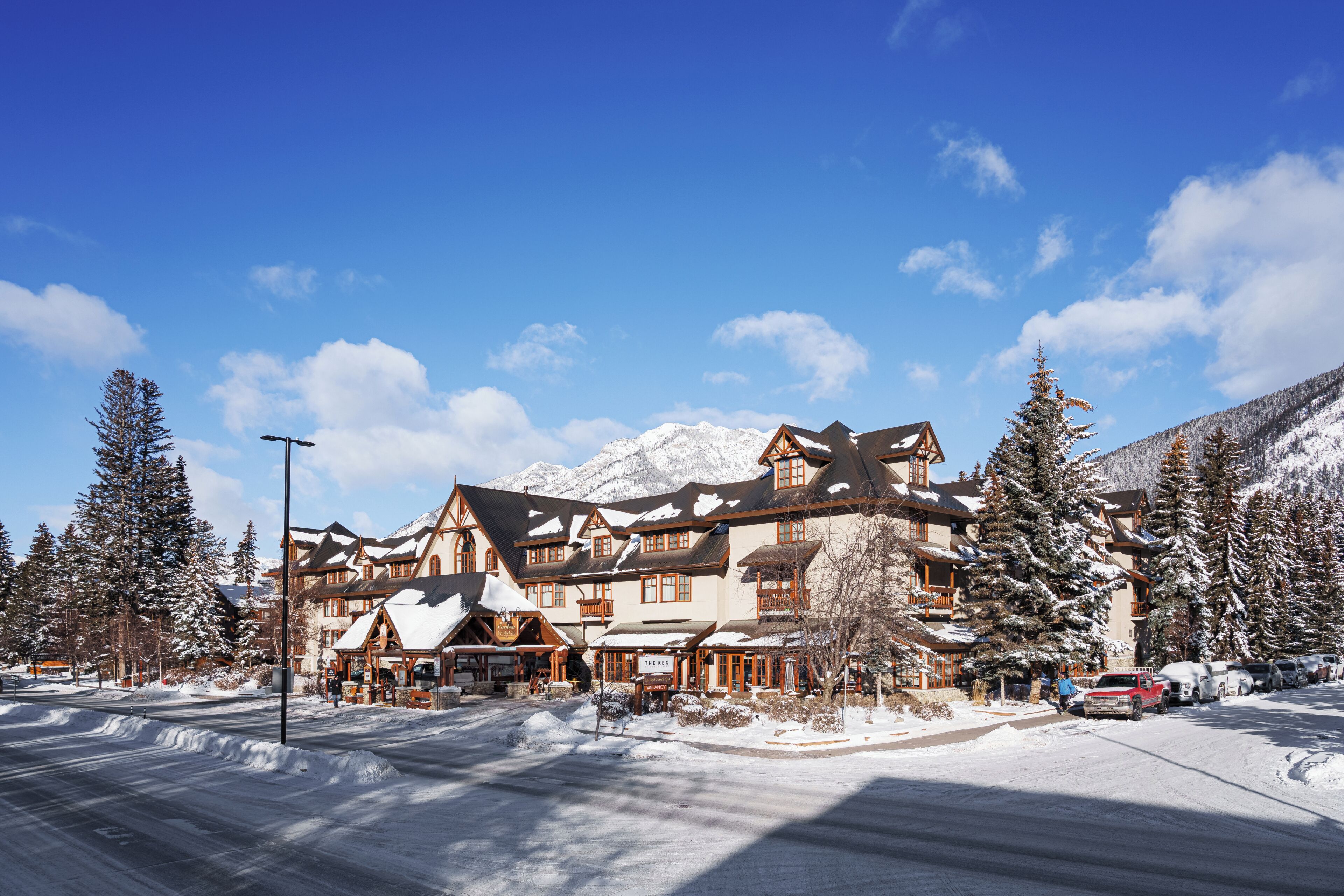 A snow-covered building with multiple stories and a traditional architectural style, surrounded by snow-laden trees and mountains in the background.