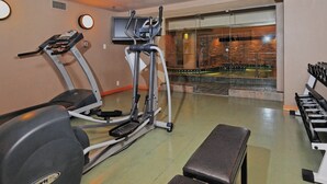 Une salle de sport équipée de matériel d’exercice, avec un banc et une vue sur une piscine à travers un mur de verre.